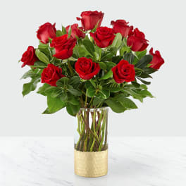 Red roses arranged in a clear glass vase with green foliage.