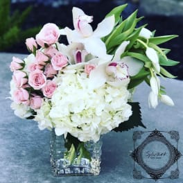 Pink roses and white orchids arranged in a clear square vase