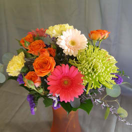 Mixed bouquet of gerbera daisies, roses, and chrysanthemums in an orange vase