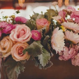 Pink and peach floral centerpiece with roses and daisies in a low container