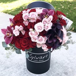 Bouquet of red and pink roses with dark purple orchids in a black hat box
