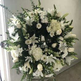 Large white funeral wreath on an easel with lilies and roses