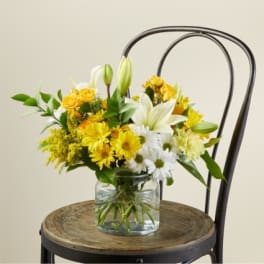 Yellow and white flowers in a clear glass vase on a chair