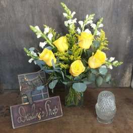 Yellow roses in a glass vase with white snapdragons and a small glass candle holder
