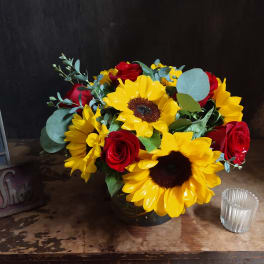 Bouquet of yellow sunflowers and red roses in a dark vase
