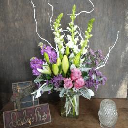 Tall bouquet of lilies, roses, and purple flowers in a glass vase