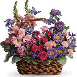 Basket arrangement of pink and purple flowers with butterfly picks
