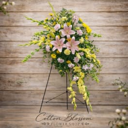 Standing floral spray with pink lilies and yellow blooms on a black easel