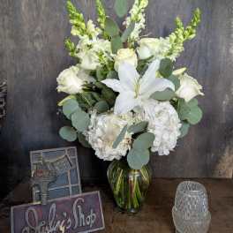 White floral arrangement in a glass vase with roses, lilies, and hydrangeas