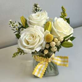 White roses and yellow accents in a glass vase with a gingham ribbon