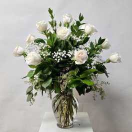 White roses in a clear glass vase with baby's breath and greenery