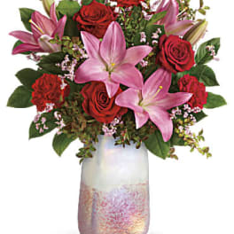 Pink lilies and red roses arranged in a tall iridescent vase