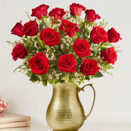 Red roses arranged in a gold pitcher vase
