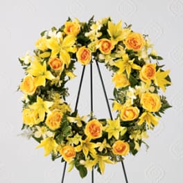 Yellow floral wreath with roses and lilies on a black stand