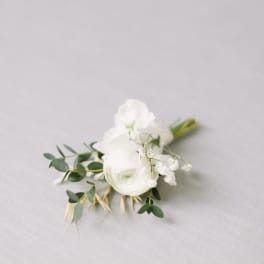 Small white floral boutonniere with greenery on a light fabric background