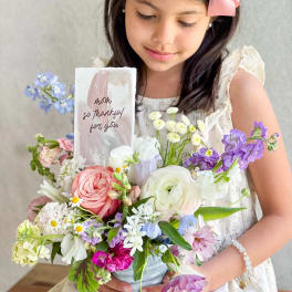 Girl holding a pastel mixed flower arrangement with a thank-you card