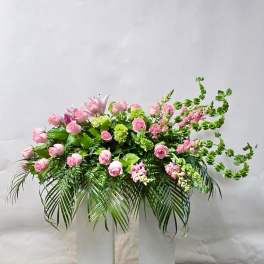 Pink roses and mixed greenery arranged in a tall white pedestal display