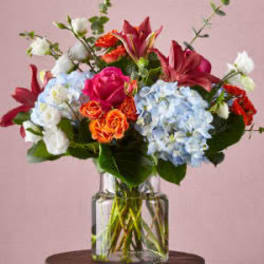 Mixed bouquet of roses, hydrangeas, and lilies in a clear glass vase