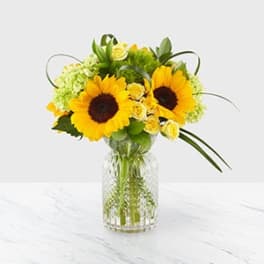 Sunflowers and yellow roses arranged in a clear glass vase