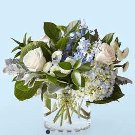 White roses and blue hydrangea in a clear glass vase