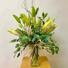 Tall lily arrangement in a clear glass vase with a raffia bow