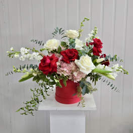 Red and white roses in a red hatbox with trailing greenery
