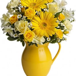Yellow and white flower arrangement in a yellow pitcher vase