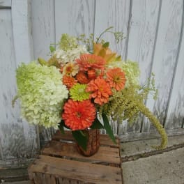 Orange and green floral arrangement in a rustic vase