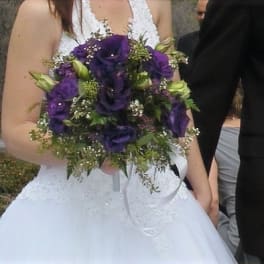 Bride holding a bouquet of purple flowers with white ribbon