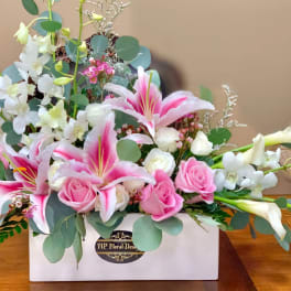 Pink lilies and roses arranged in a white box with white orchids