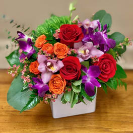 Bouquet of red and orange roses with purple orchids in a white vase