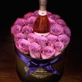 Pink roses arranged around a champagne bottle in a round box