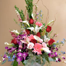 Large mixed bouquet of roses, lilies, orchids, and gerbera daisies in a white vase