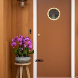 Potted purple orchids on a small wooden stool beside a front door