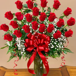Red roses arranged in a clear glass vase with a large red bow