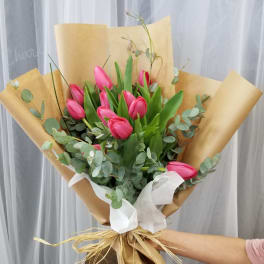Pink tulip bouquet wrapped in brown paper with white ribbon