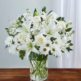 White lilies, roses, and daisies arranged in a clear glass vase