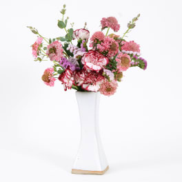 Pink and red mixed flowers arranged in a tall white vase