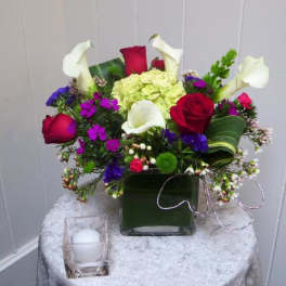 Mixed bouquet with red roses, white calla lilies, and purple flowers in a square vase