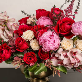 Bouquet of red and pink roses with pale orchids in a gold vase