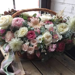 Basket arrangement of pink and white roses with mixed blooms and ribbon
