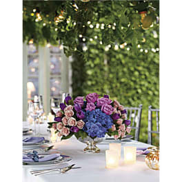 Purple and pink floral centerpiece in a silver vase on a table