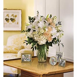 White lilies and peach roses arranged in a glass vase on a table