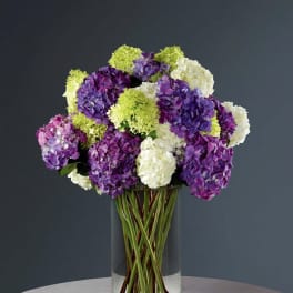 Purple, white, and green hydrangeas in a clear glass vase