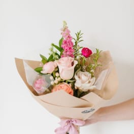 Hand-tied bouquet of pink and white roses wrapped in beige paper