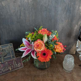 Mixed bouquet in a glass vase with roses, lilies, and orange gerbera daisies