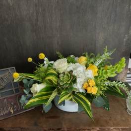 Low floral arrangement with white and yellow blooms in a white container