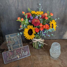 Bouquet of sunflowers, orange roses, and red mums in a glass vase