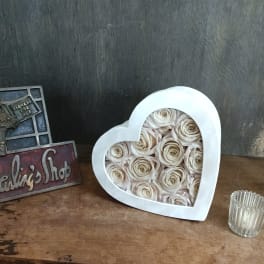 Heart-shaped box filled with cream roses beside a decorative shop sign