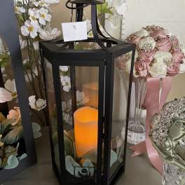 Black lantern with an orange candle surrounded by white flowers and satin ribbon bouquets